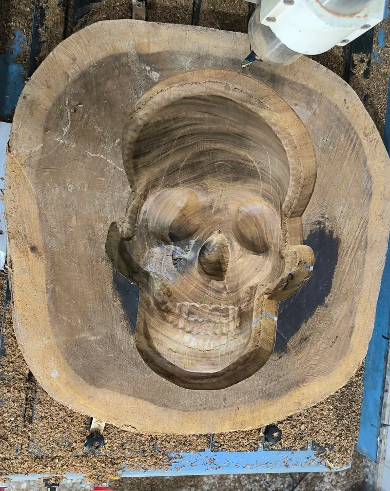 Calavera tallada en 3D dentro de un tronco de madera, sobre la mesa de la router CNC